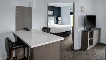 A hotel room with a desk, chairs, a bed, a TV, and a door leading to another room.