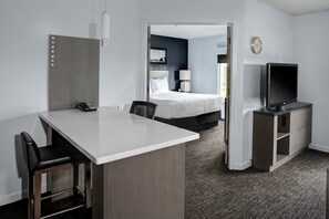 Una habitación de hotel con escritorio, sillas, cama, televisor y una puerta que da a otra habitación.