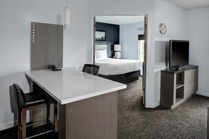 Una habitación de hotel con escritorio, sillas, cama, televisor y una puerta que da a otra habitación.
