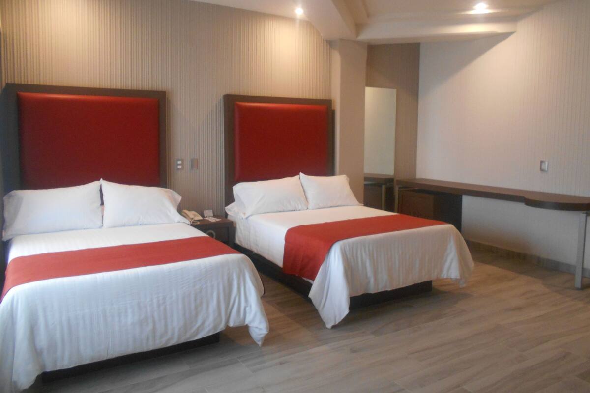 A hotel room with two beds, each with a red headboard, white bedding, and a wooden floor.