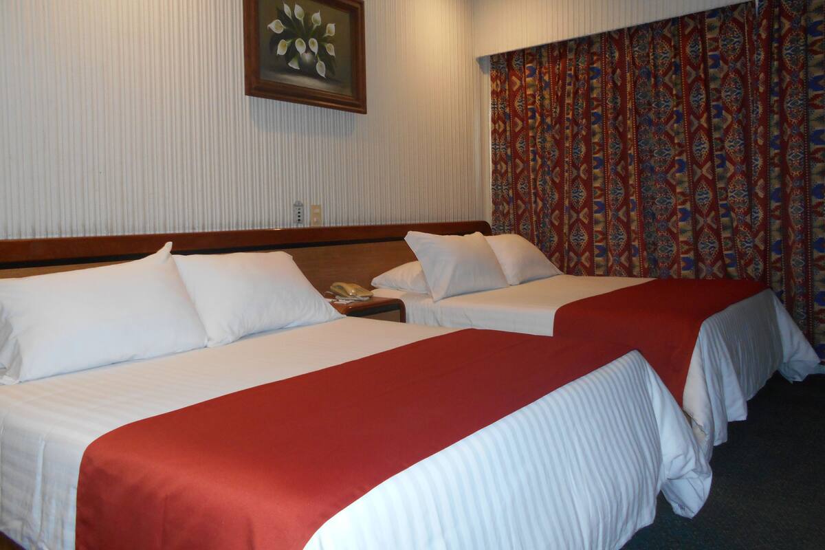 A hotel room with two beds, a wooden headboard, a telephone on the nightstand, and a patterned curtain.