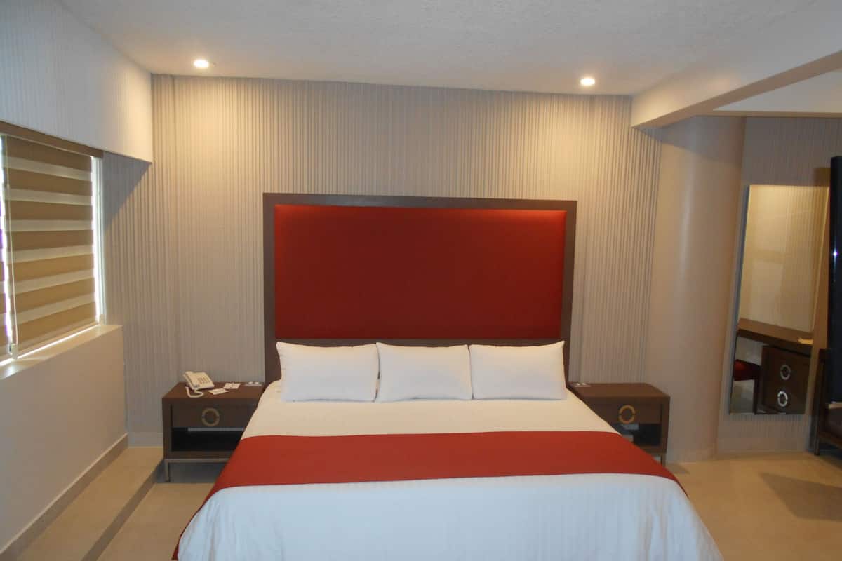 A hotel room with a large bed, a bedside table with a phone, a nightstand, and a mirror.