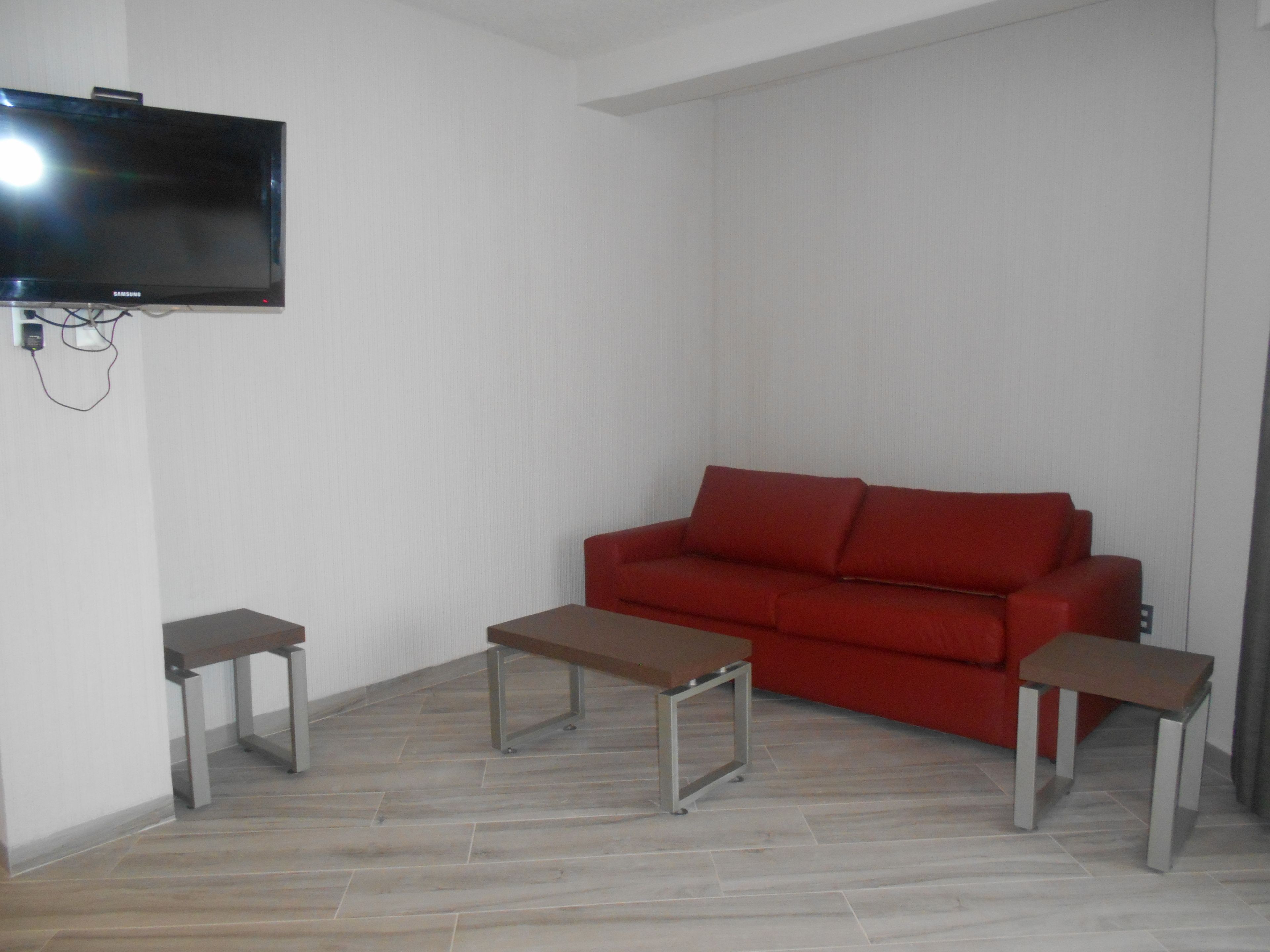 A living room with a red sofa, two small tables, and a mounted TV on the wall.