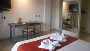 Una habitación de hotel con cama, escritorio, silla, televisión y espejo.