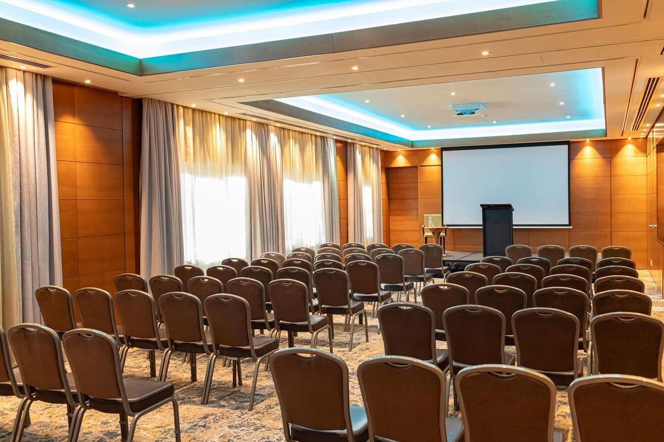A conference room with rows of chairs, a podium, and a large screen.