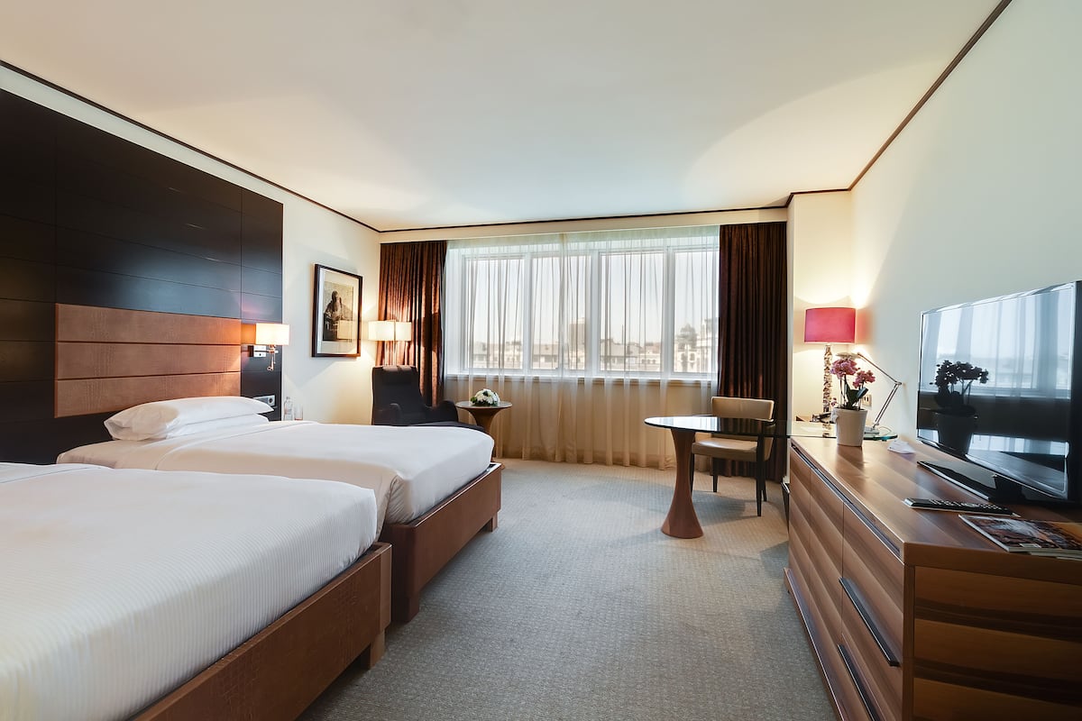 Ein Hotelzimmer mit zwei Betten, einem Schreibtisch, einem Fernseher und einem Fenster mit Vorhängen.