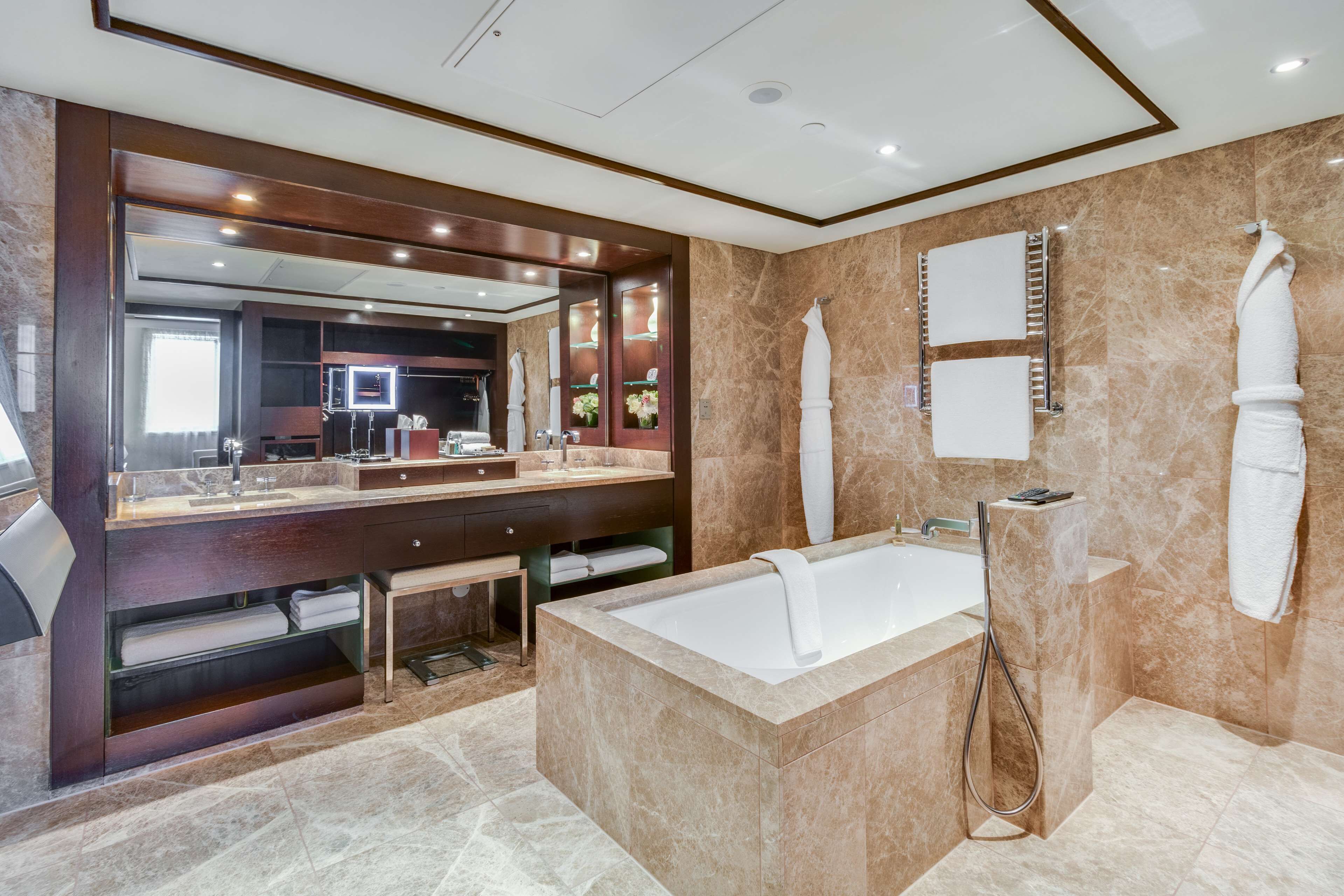 A modern bathroom with a large mirror, a bathtub, a shower, and a vanity with a sink and towel rack.