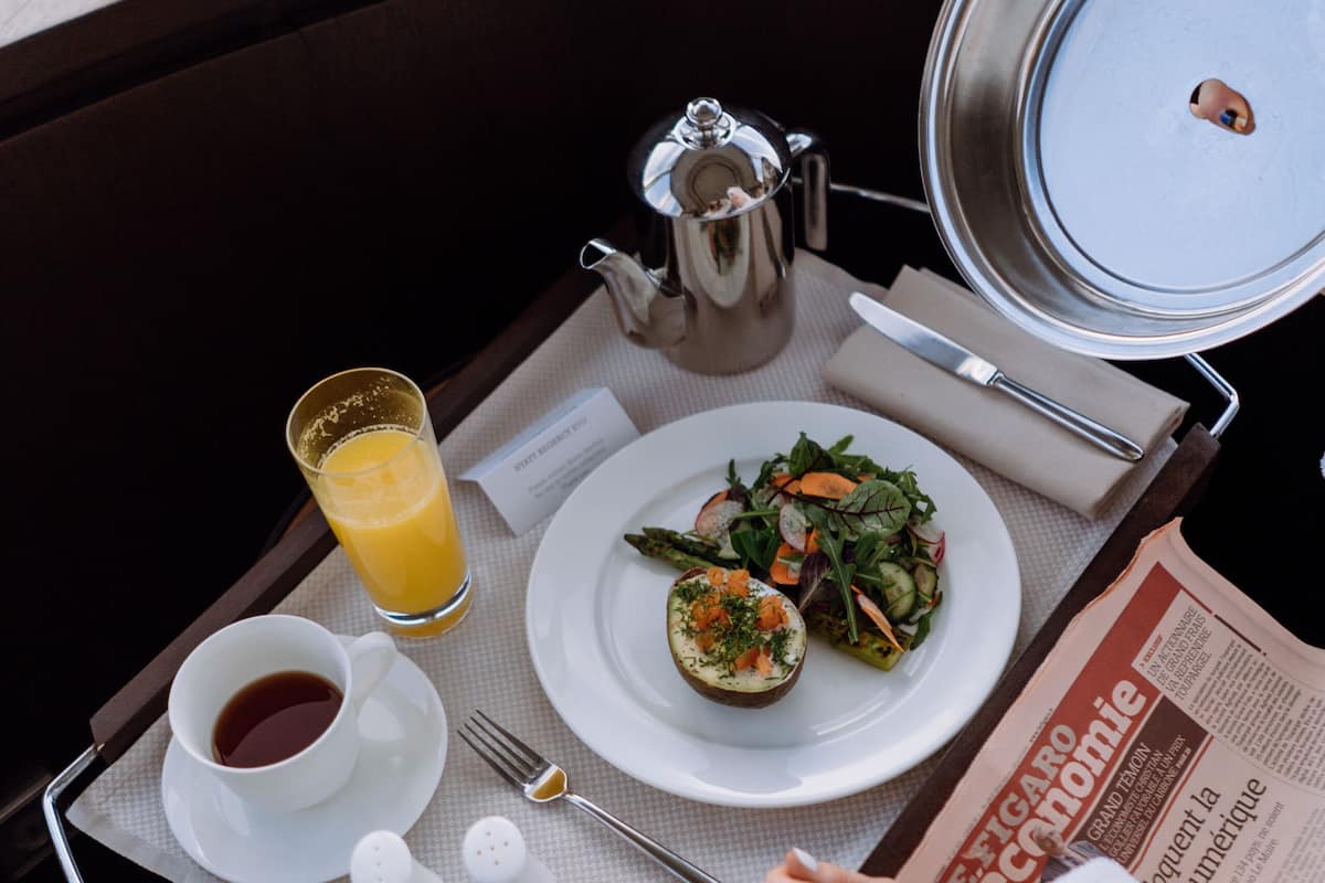 Ein Frühstücksbrett mit Speisen, einem Orangensaftglas, einer Kaffeetasse, Salz- und Pfefferstreuern sowie einer Zeitung.