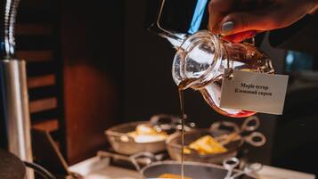A person pouring maple syrup onto a waffle on a white plate.