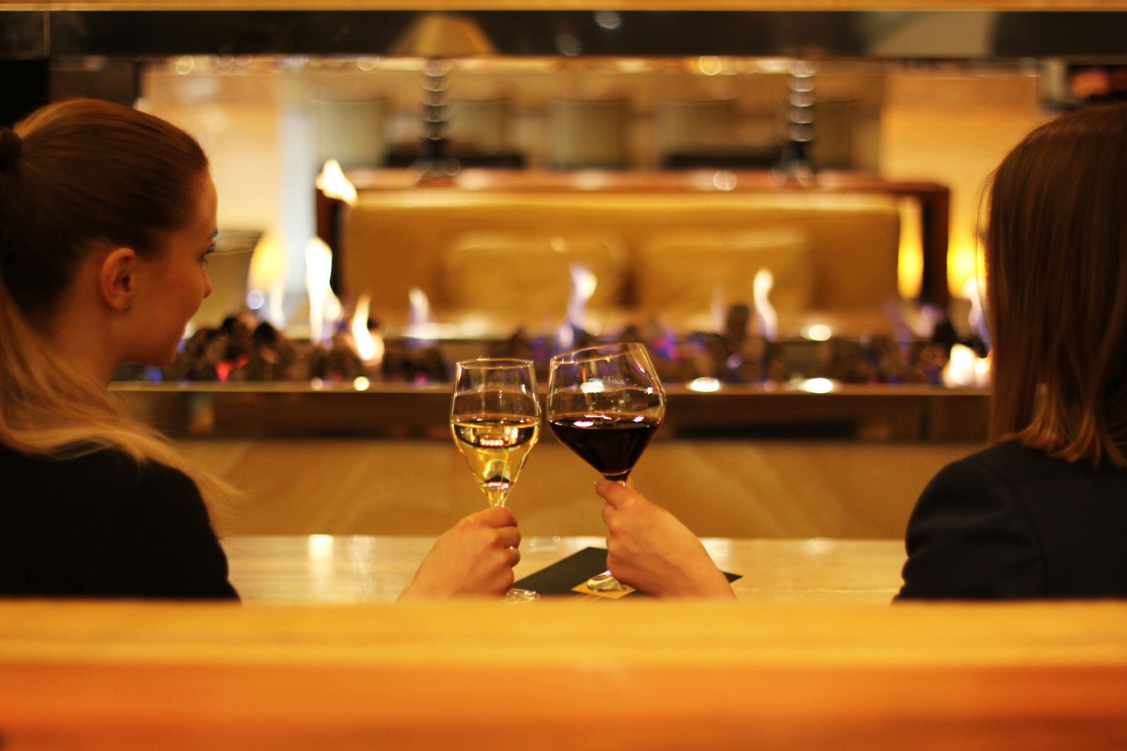 Dos personas sentadas a una mesa con copas de vino, en un restaurante con un bar al fondo.