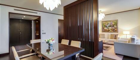 A modern hotel room with a glass dining table, comfortable seating, a wooden accent wall, and a cozy seating area with a sofa and lamp.