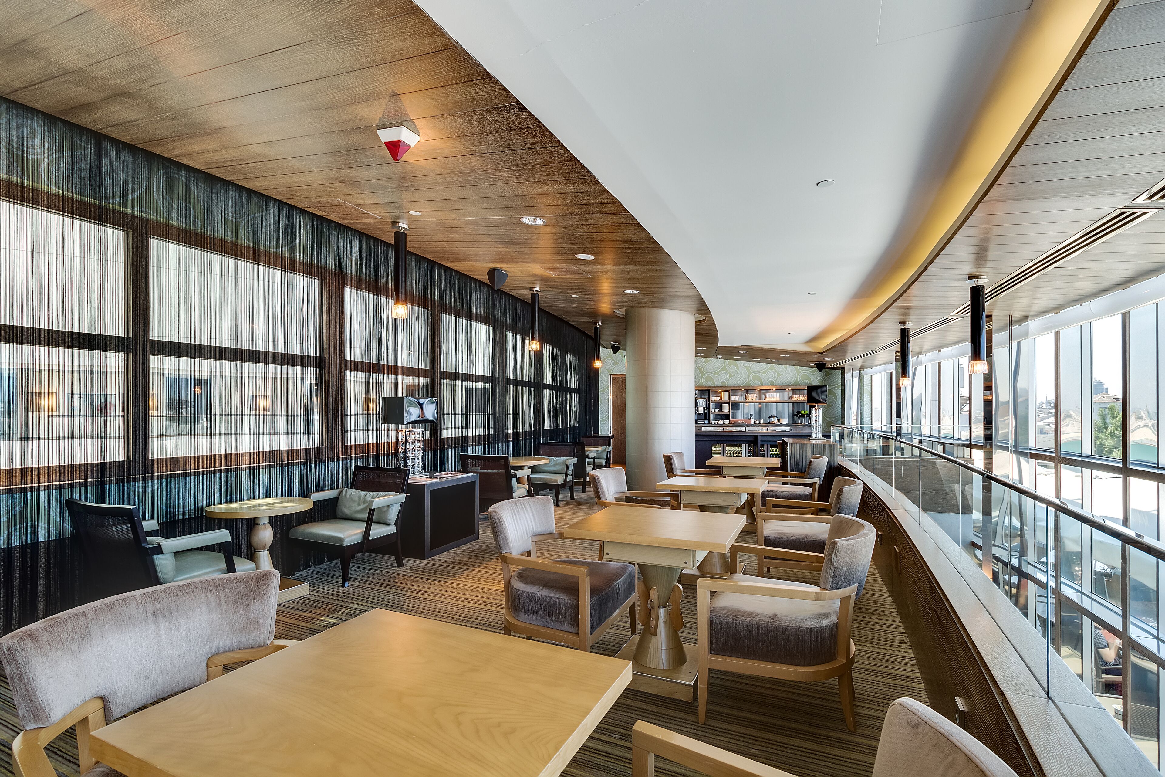 En moderne hotellobby med trægulv, store vinduer og et barområde.