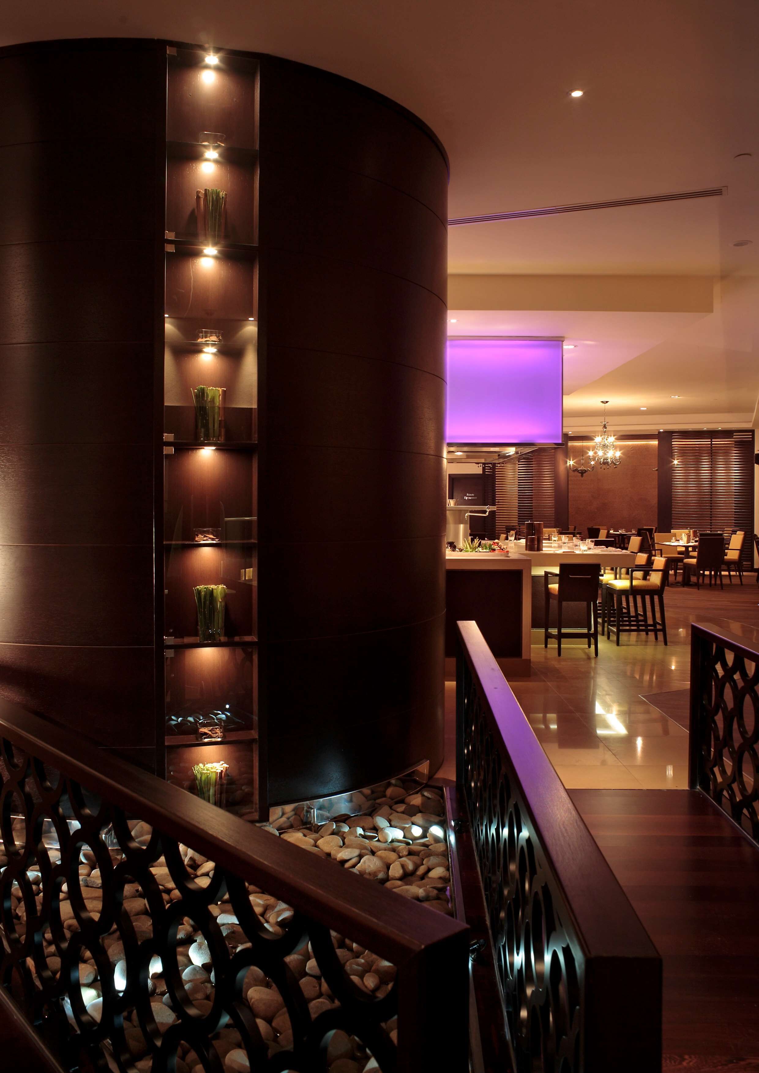 A modern hotel lobby with a curved reception desk, a seating area with tables and chairs, and a decorative wall with plants and lights.