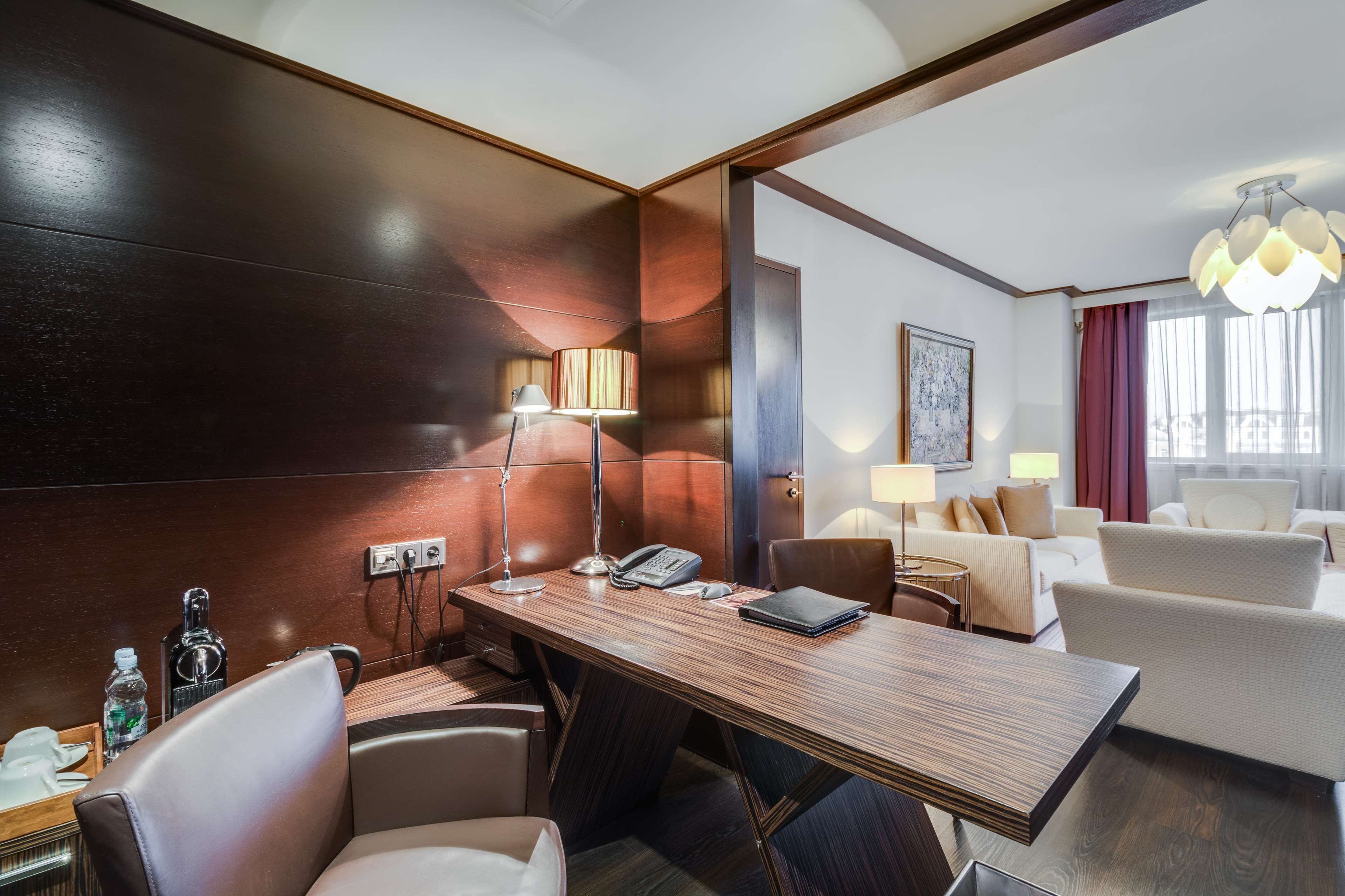 Una habitación de hotel con un escritorio de madera, sillones de cuero, un sofá y una araña.