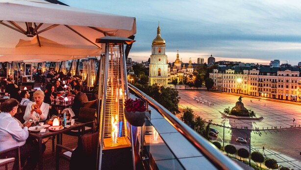 A rooftop dining area with tables and chairs, overlooking a cityscape with a prominent building with golden domes. - Hyatt Regency Kyiv (Kyiv)