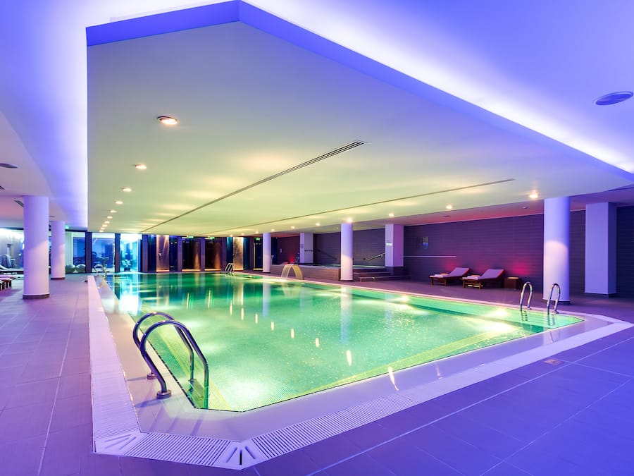 An indoor swimming pool with clear water, surrounded by lounge chairs and a modern ceiling design.