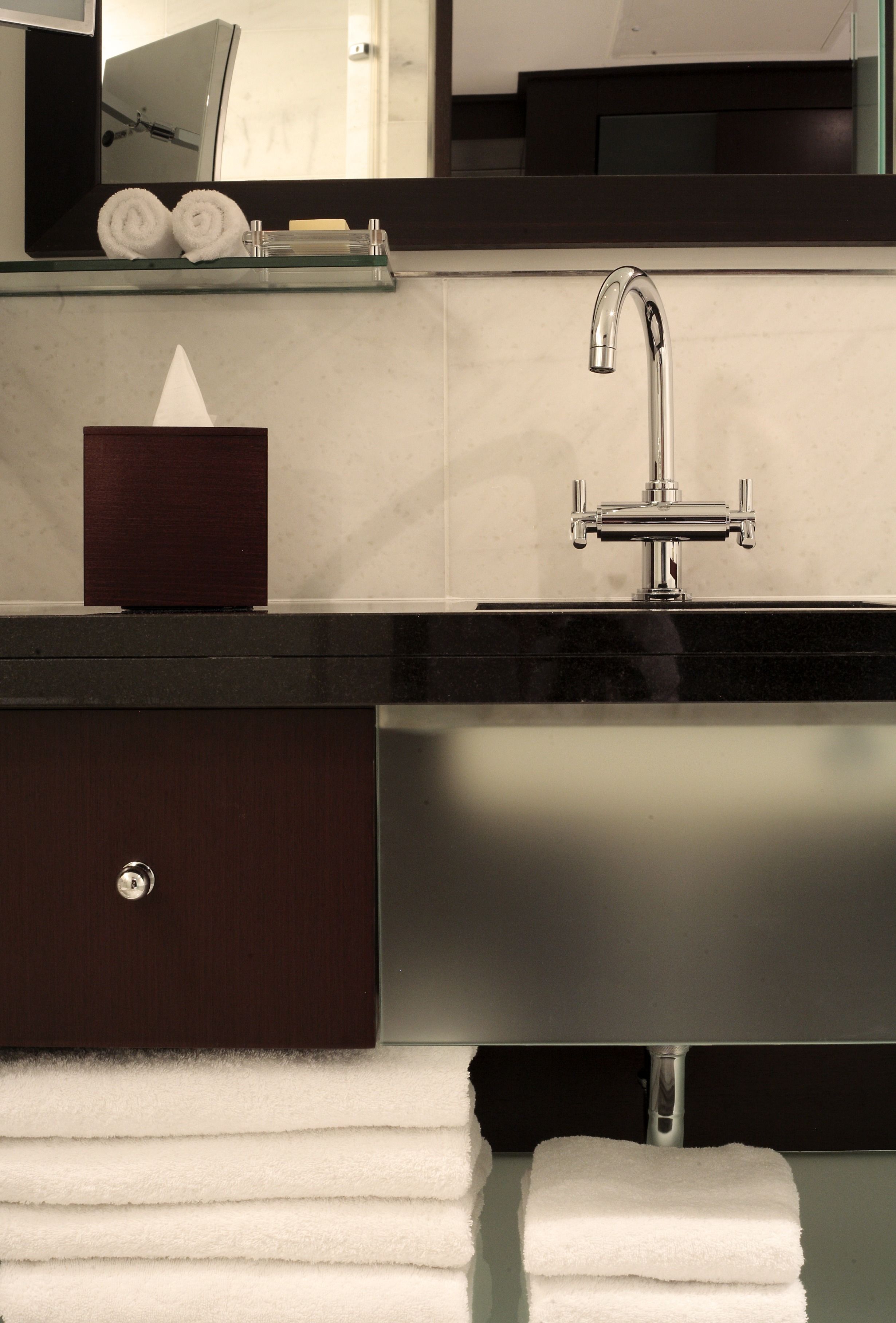 A modern bathroom with a dark wood vanity, a glass shelf with towels, and a large mirror above the sink.