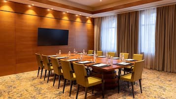 A conference room with a large table, chairs, a flat-screen TV, and a window with curtains.
