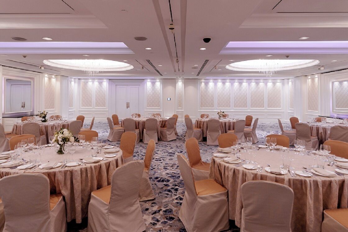 Een balzaal met ronde tafels, stoelen en kroonluchters.