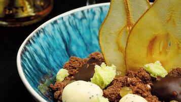 Un piatto dessert con diversi condimenti, tra cui un dolce al cioccolato, una fetta di pera e un oggetto sferico bianco.