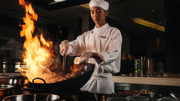 A chef cooking with a wok over an open flame in a professional kitchen setting. - Hyatt Regency Kyiv (Kyiv)