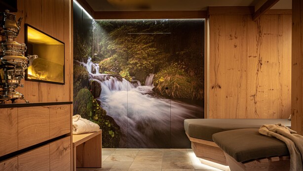 A spa room with a wooden interior, a large wall mural of a waterfall, a massage table, and a tea set on a wooden cabinet. - Hotel Rosa degli Angeli (Pejo)
