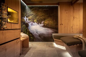 Een spa-ruimte met houten inrichting, een groot muurschilderij van een waterval, een massagetafel en een theesetje op een houten kast.
