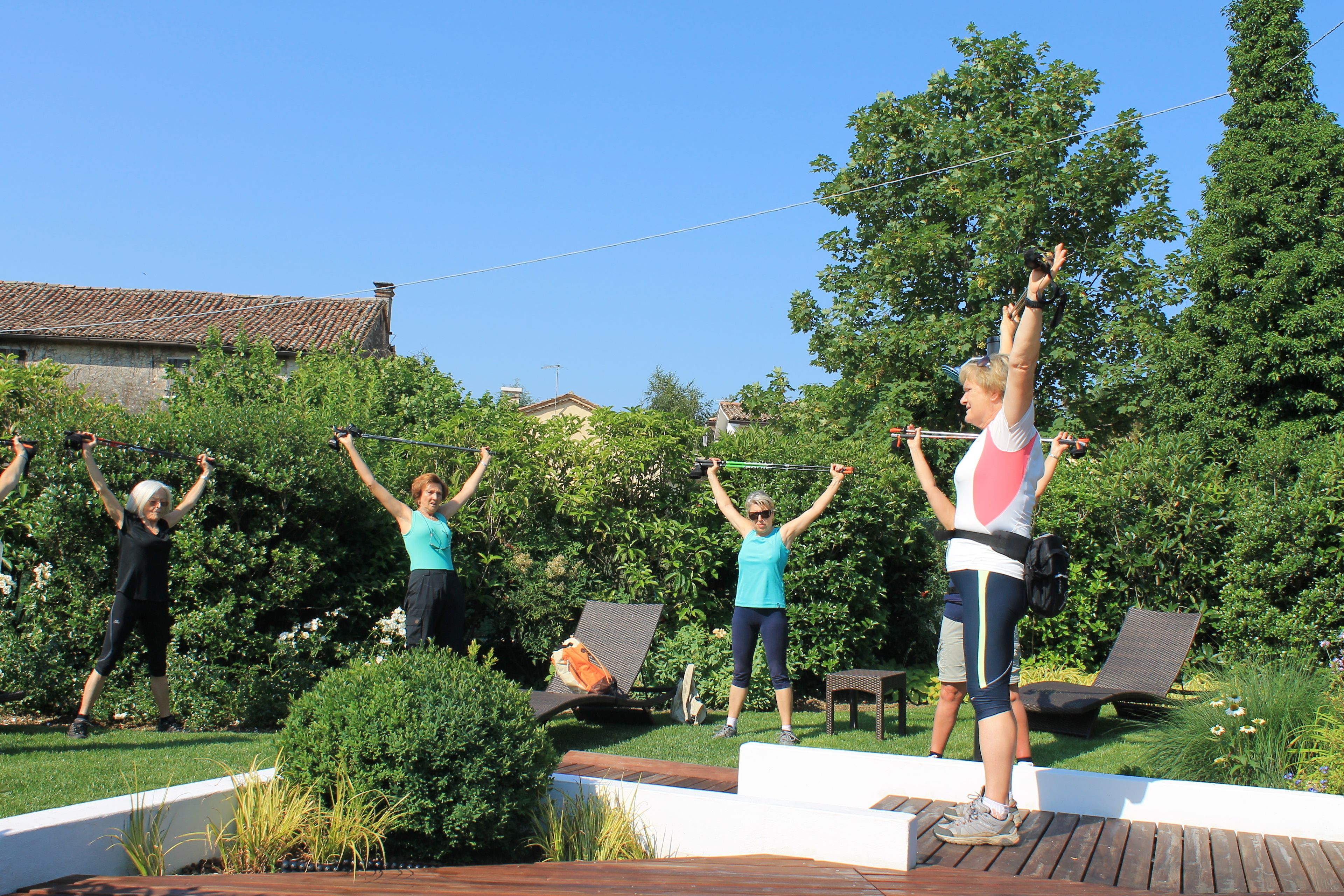 Un gruppo di persone che si allena all'aperto, con un giardino e poltrone relax sullo sfondo.