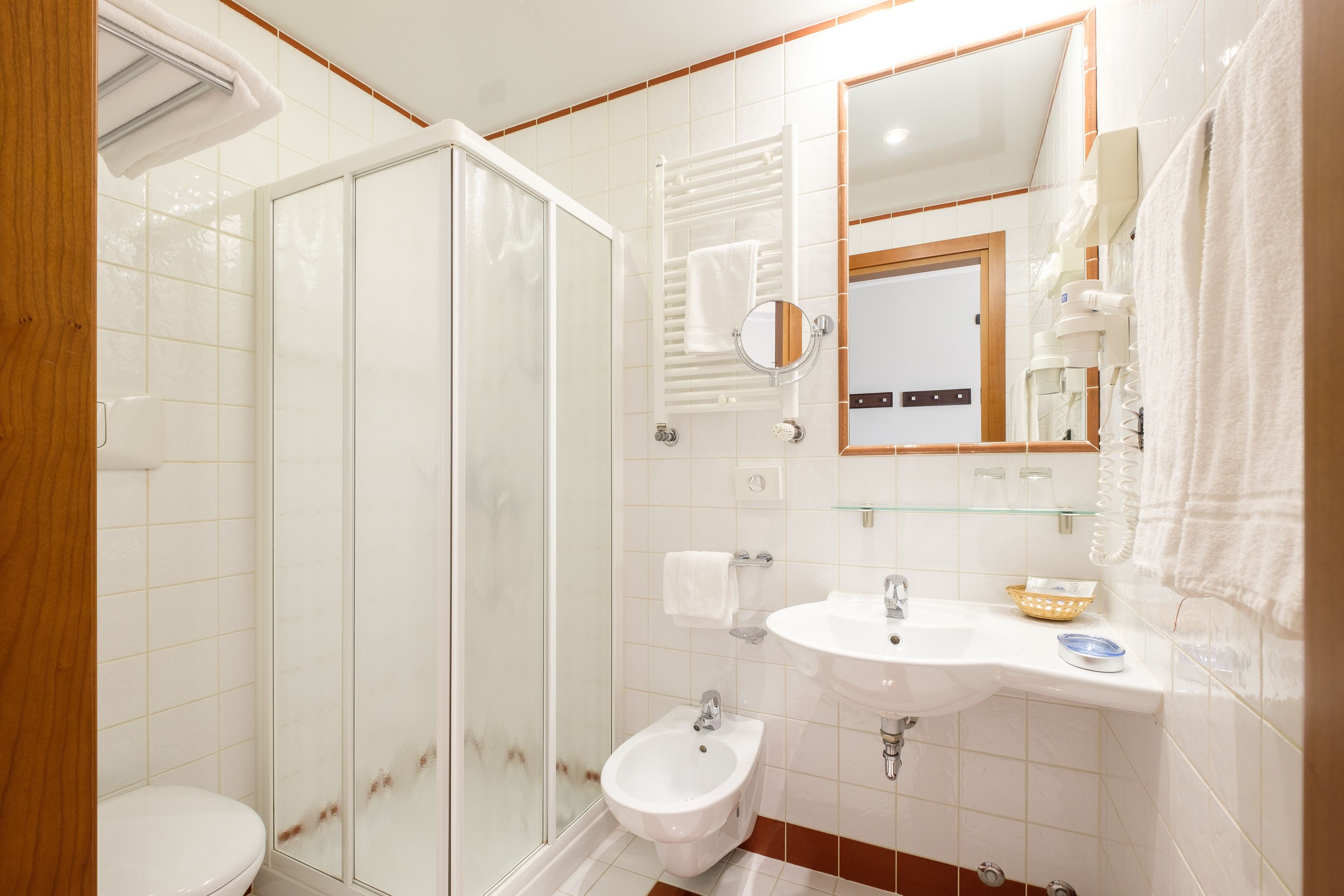 Un baño con cabina de ducha de vidrio, un bidé, un lavabo con espejo y un perchero para toallas.