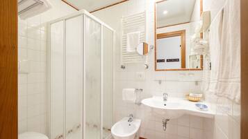 Un baño con cabina de ducha de vidrio, un bidé, un lavabo con espejo y un perchero para toallas.