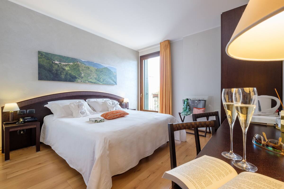 Habitación de hotel con una cama grande, un escritorio con dos copas de champán y un cuadro en la pared.