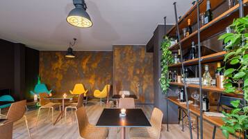 A modern dining area with a black table, patterned chairs, and a wooden bookshelf with bottles.