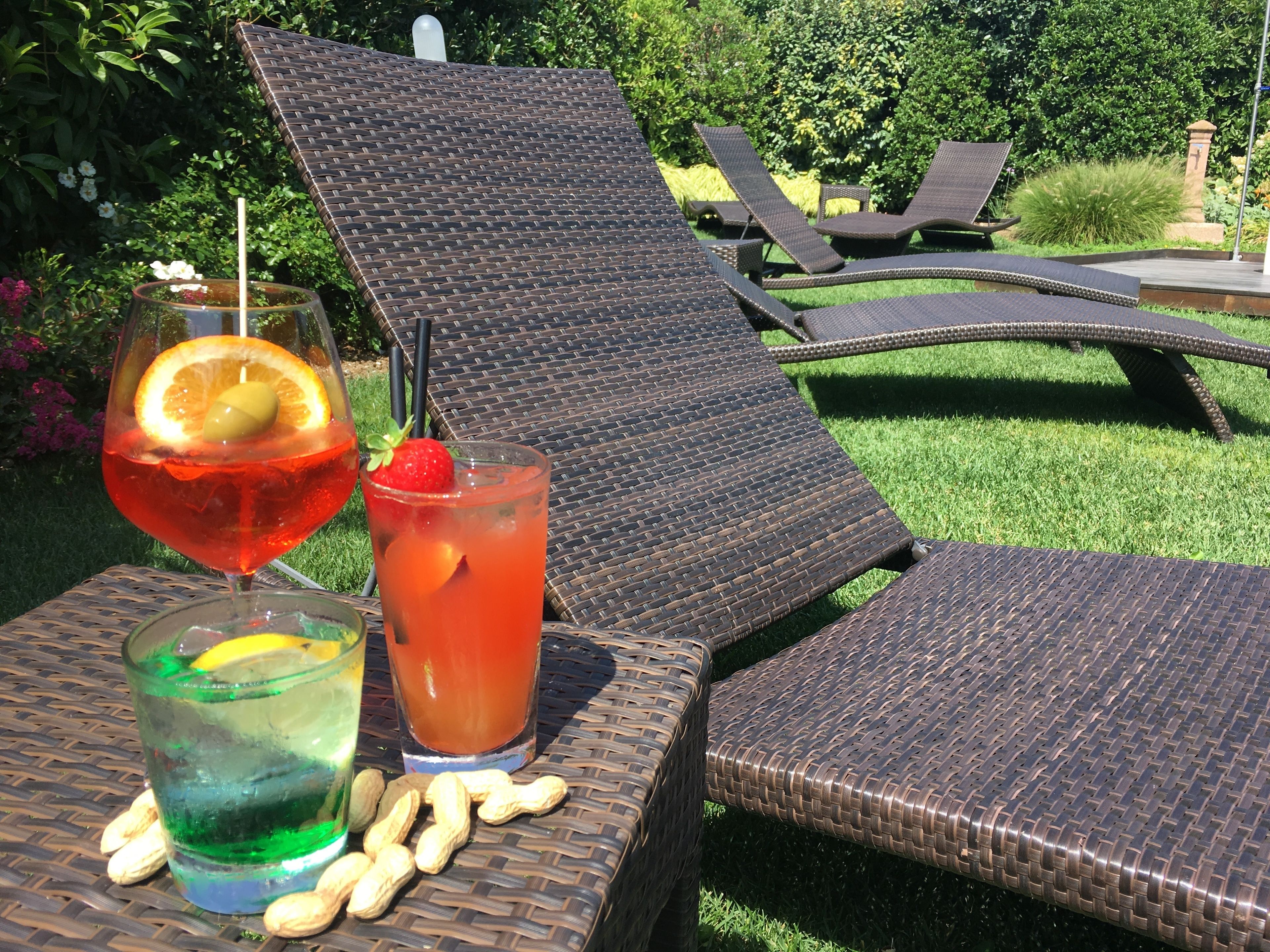 Une terrasse avec des fauteuils de jardin en osier, une table avec des boissons et, en arrière-plan, un jardin luxuriant.