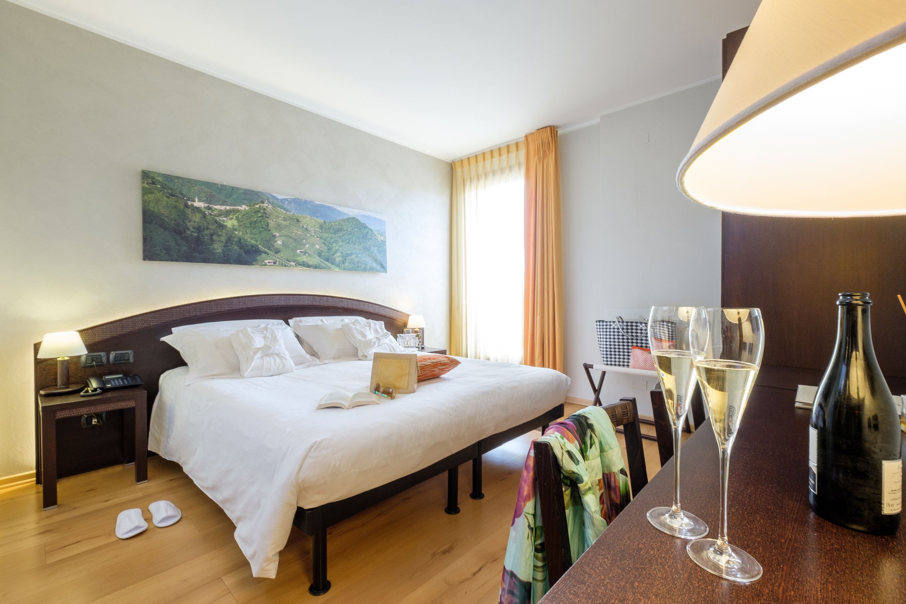 Ein Hotelzimmer mit einem Bett, einem Nachttisch, einem Tisch mit Gläsern und einer Flasche sowie einem Bild an der Wand.