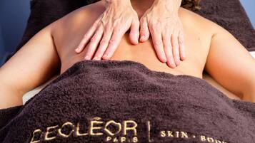 Uma pessoa recebendo uma massagem nas costas com uma toalha com a inscrição 'DELEOR PARIS'.