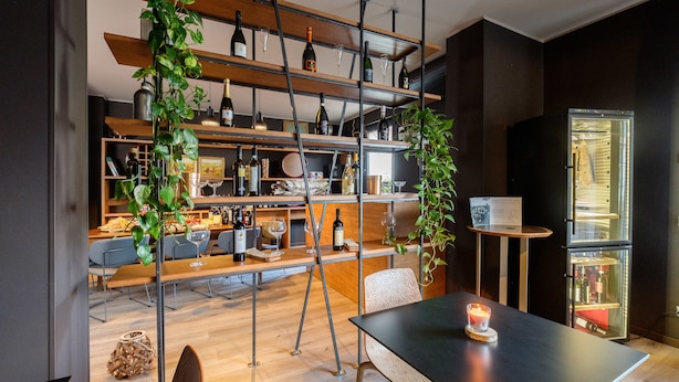 A modern interior with wooden shelves, hanging plants, and a table with a candle.