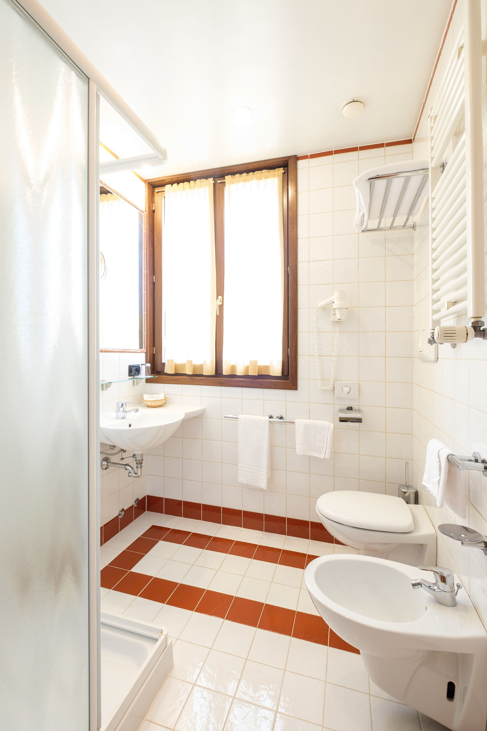 A bathroom with a sink, toilet, bidet, and a window with curtains.