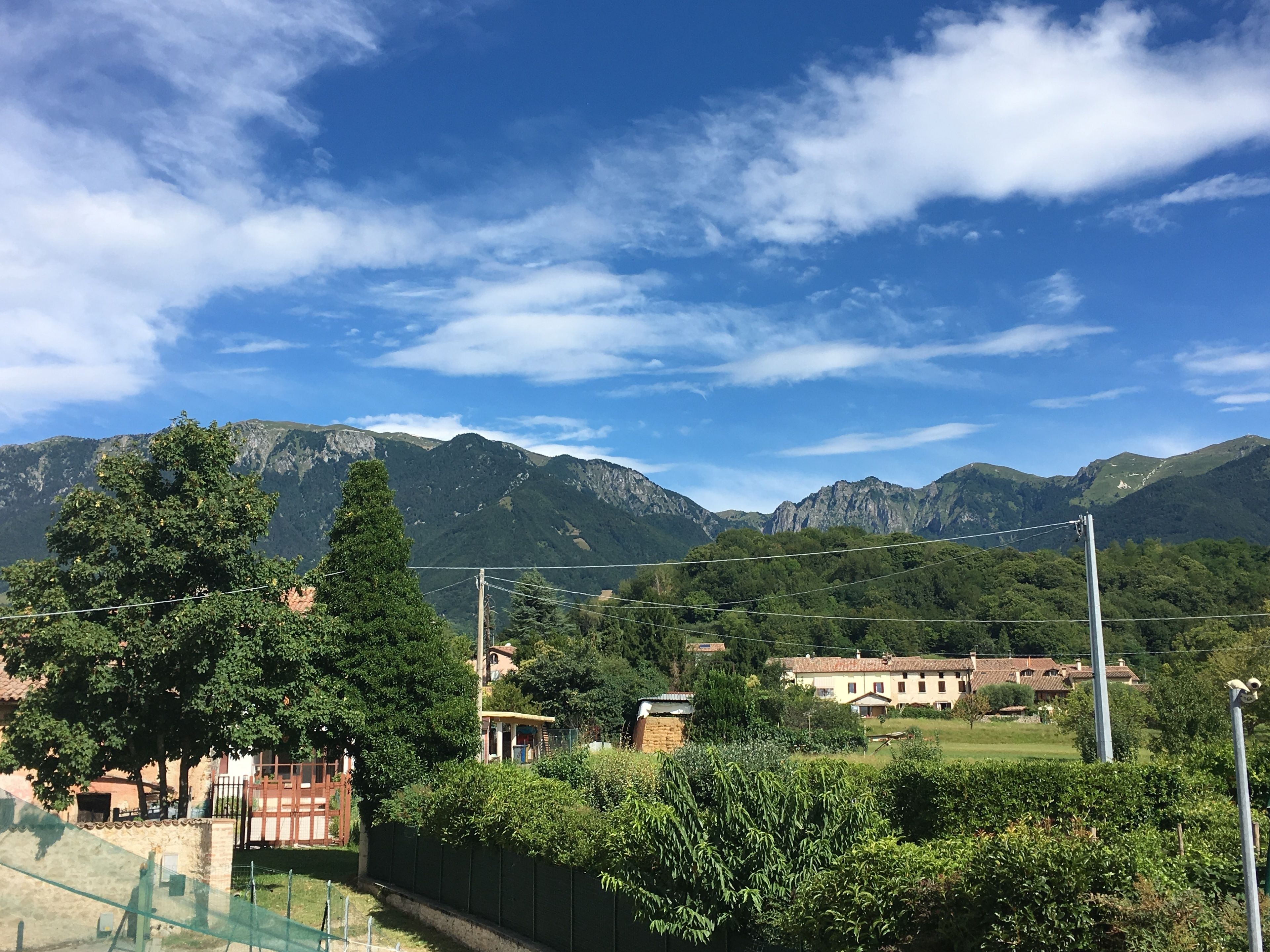 Paisaje montañoso con cielo despejado, un área cercada con árboles y edificios al fondo.