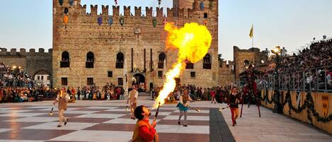 Un castillo medieval con un suelo a cuadros, una multitud de espectadores y artistas con antorchas encendidas.