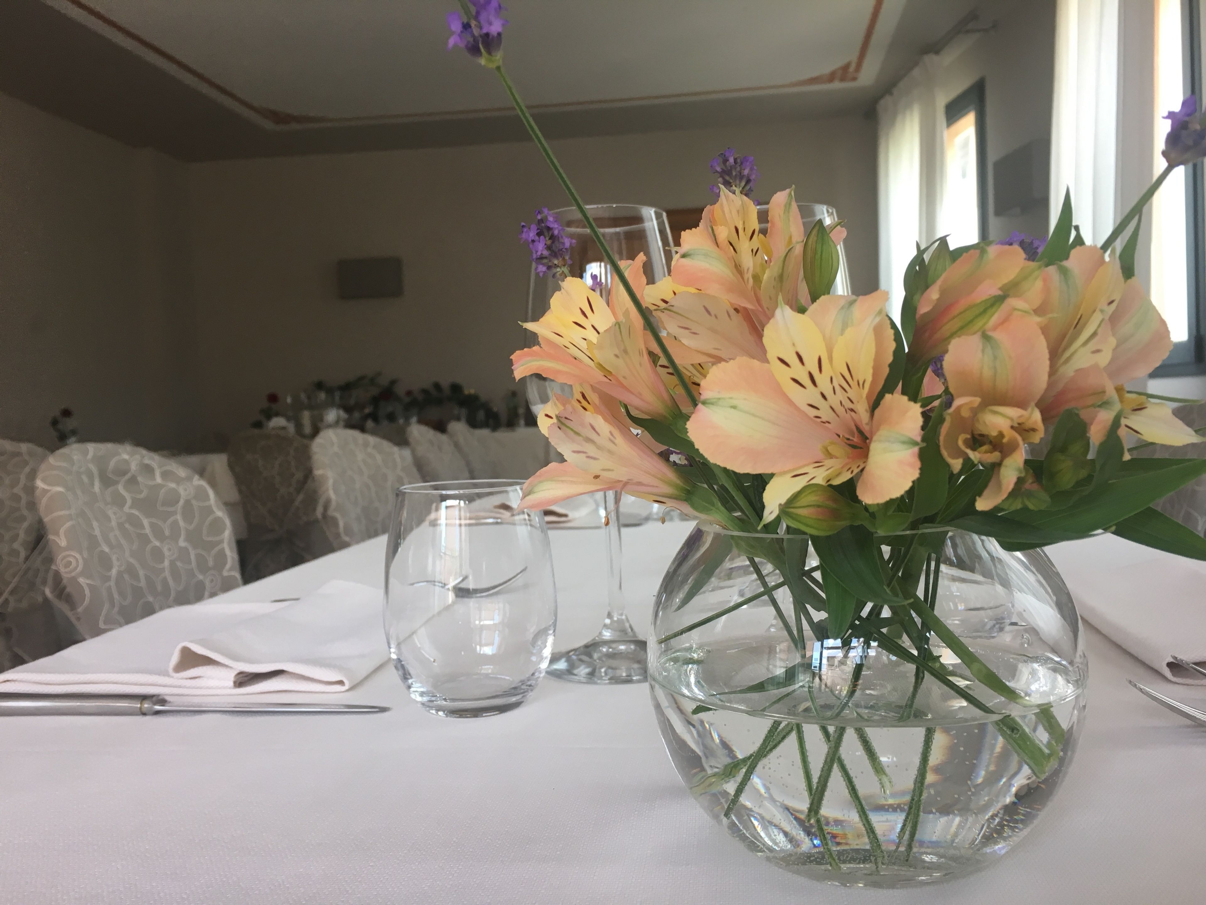 Une table à manger avec un vase de fleurs, un verre d’eau et une serviette.