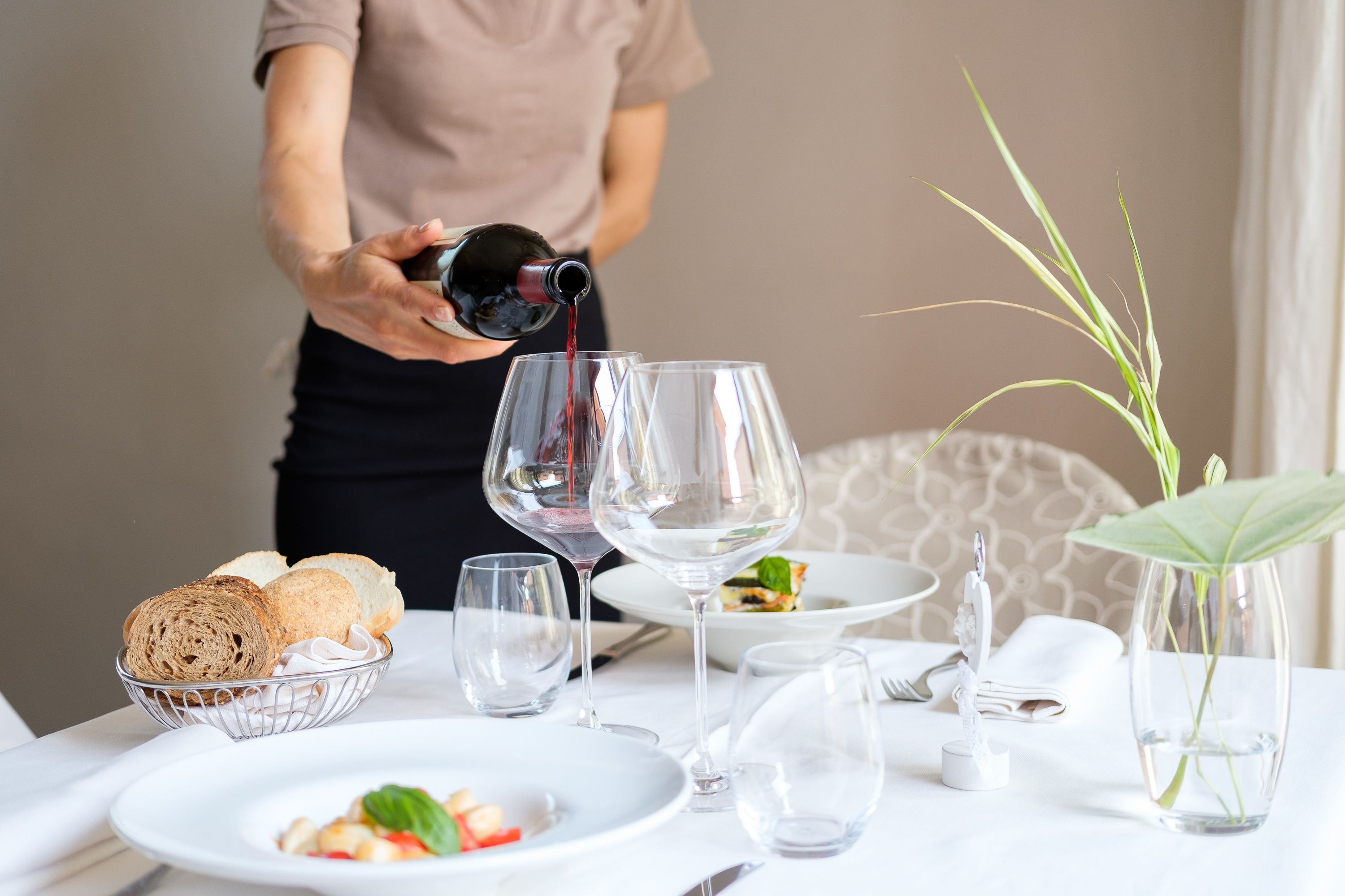 Une table mise pour un repas, avec des verres à vin, un panier de pain et un vase avec une plante.