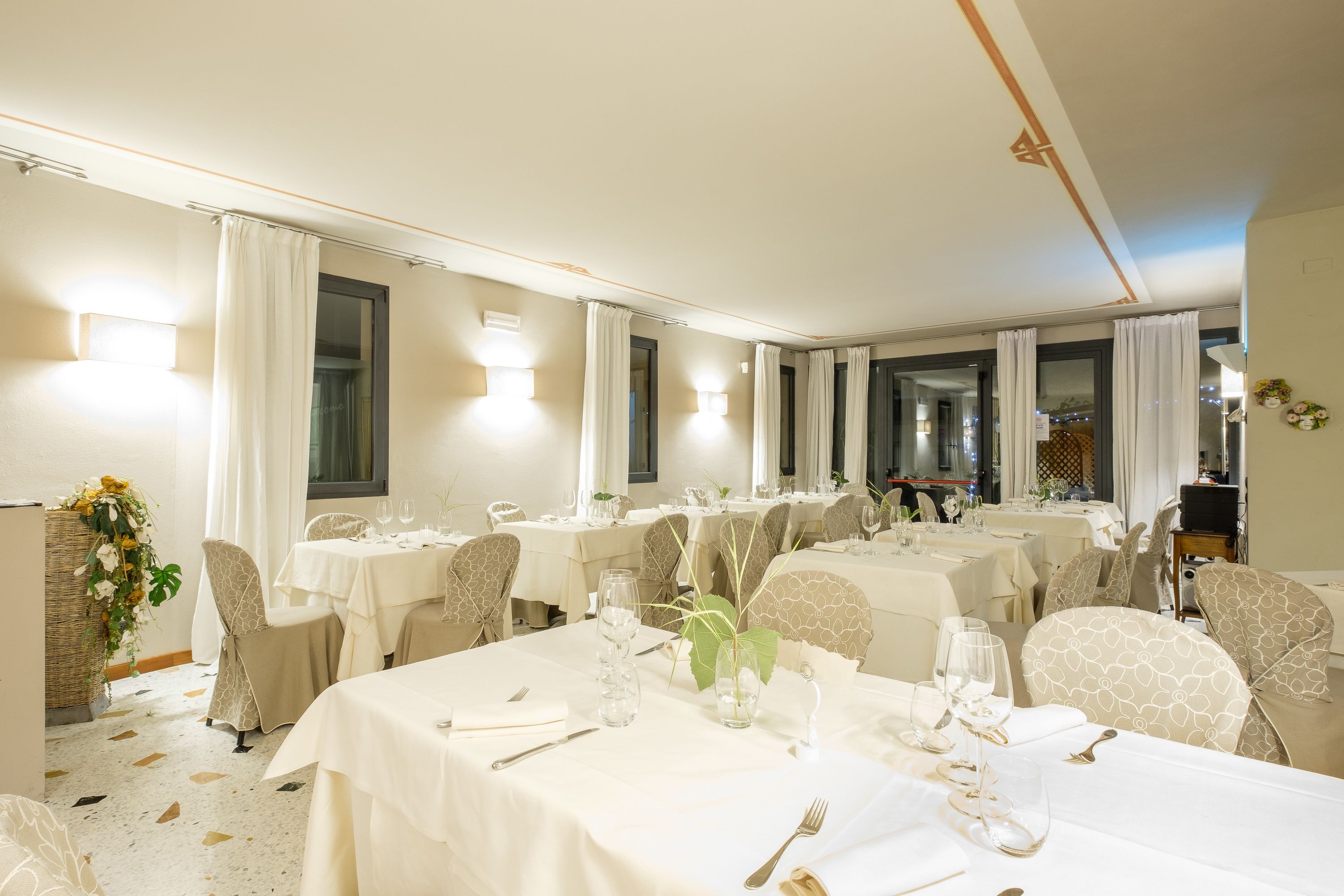 Un comedor de hotel con varias mesas dispuestas para comer, cada una con sillas, manteles y cristalería.
