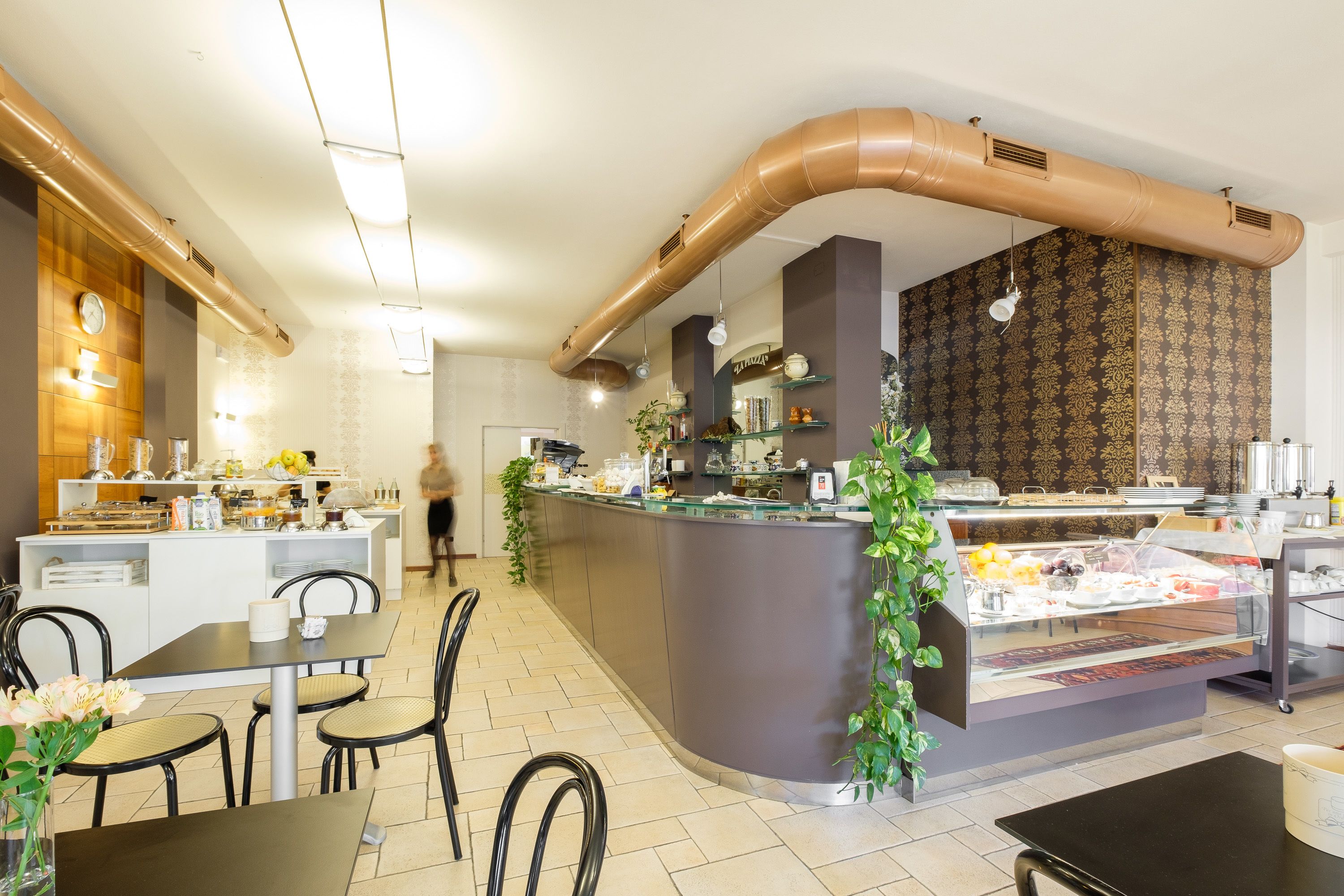 A modern cafe with a central counter, seating area, and a visible kitchen in the background.