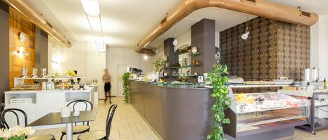 Un café moderno con mostrador central, zona de mesas y una cocina a la vista.