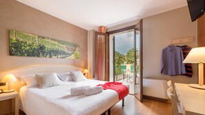 A hotel room with a large bed, a desk, a chair, a TV, and a painting of a vineyard.
