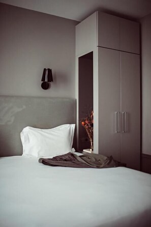 Una habitación de hotel con cama, armario, lámpara de pared y un florero con flores.