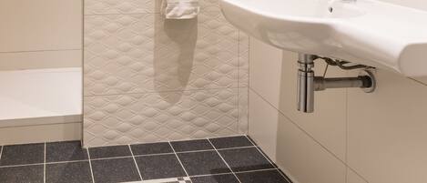 Une salle de bain avec un lavabo blanc, une serviette suspendue à un porte-serviettes et un espace douche.