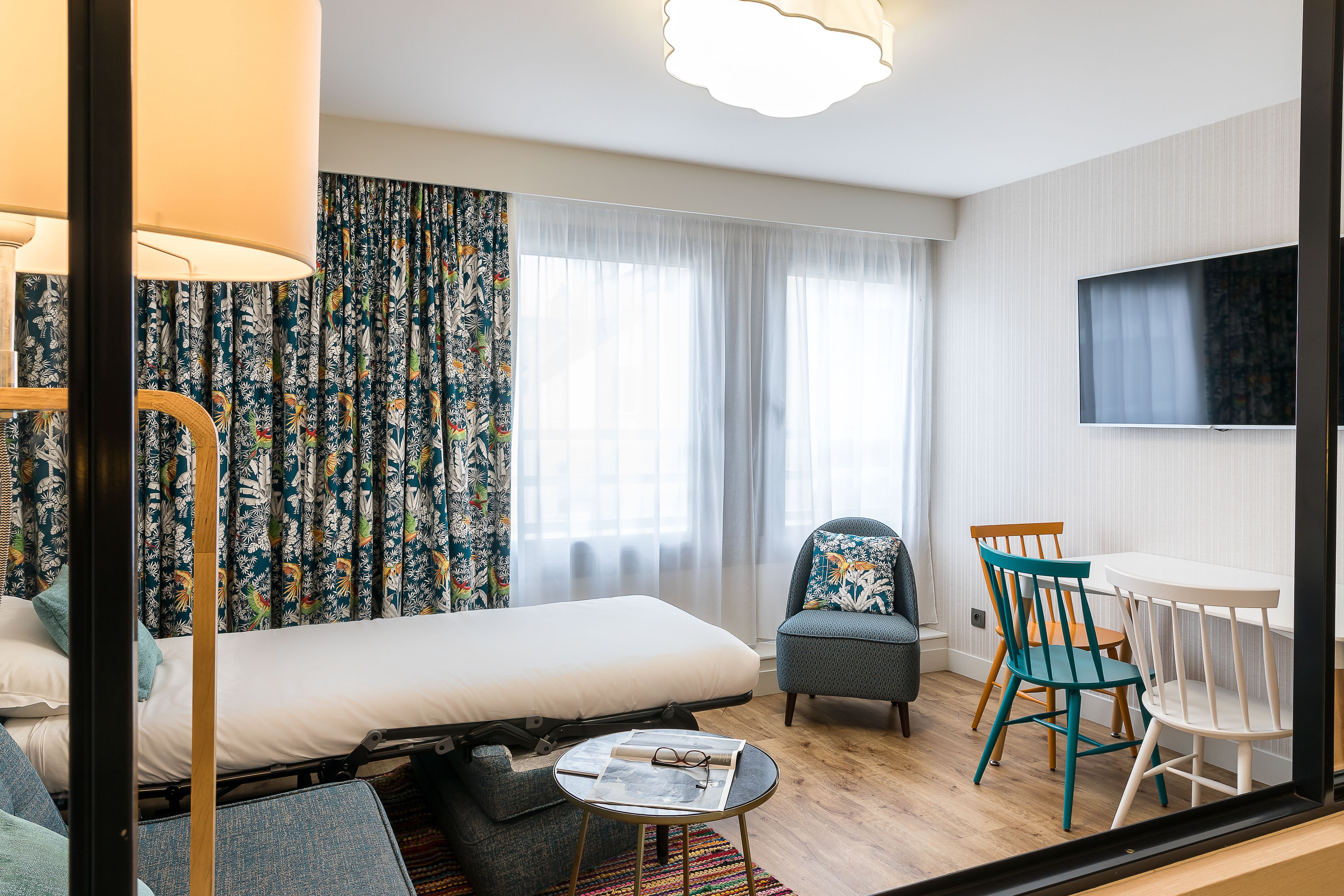Una habitación de hotel con una cama, dos sillas, una mesita y un televisor montado en la pared.