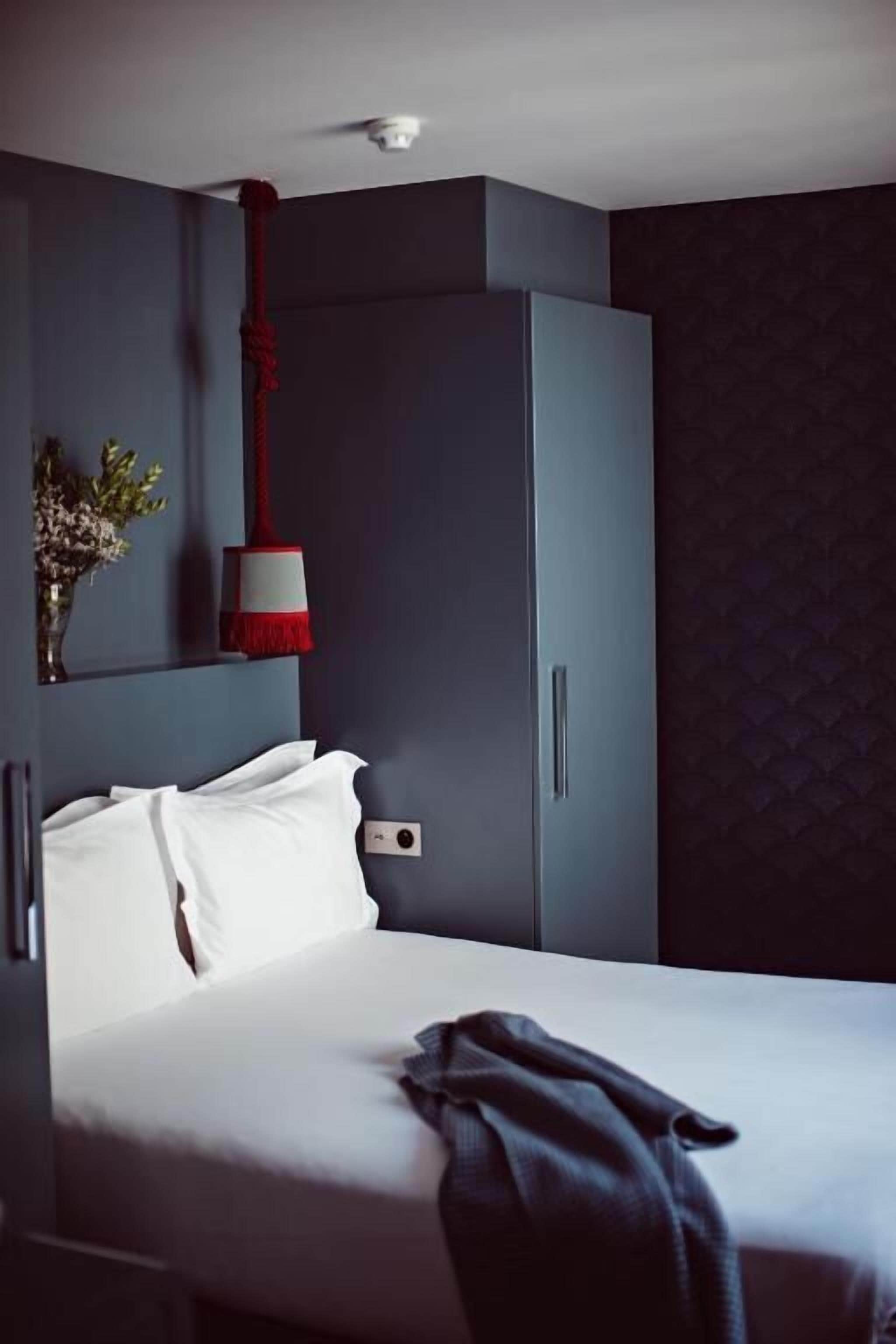 Une chambre d’hôtel avec un lit, une armoire, une lampe rouge et blanche et un luminaire fixé au mur.