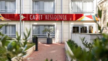 Un immeuble avec une enseigne indiquant « RÉSIDENCE CADET » et un chemin menant à l’entrée.